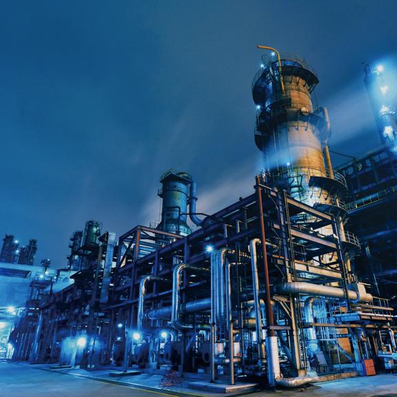 Industrial refinery with illuminated processing towers, pipelines and metal structures at night.