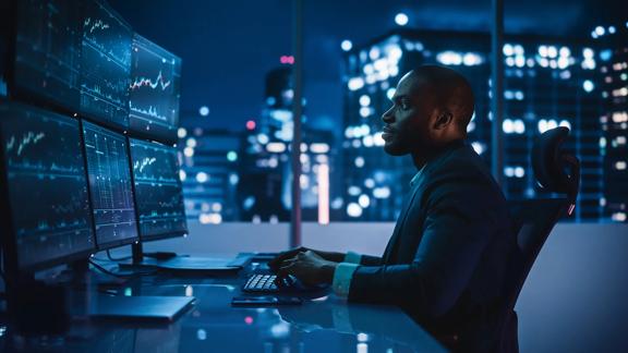 Finance professional looking at 6 screens in dark office