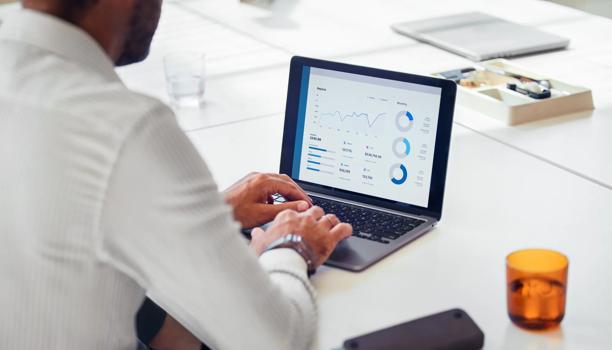 Person working on a laptop displaying business analytics charts and graphs in a modern office setting.