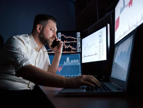 Operador de ações focado, analisando dados de mercado em vários monitores enquanto fala ao telefone