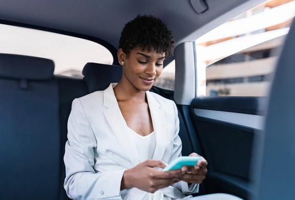 Confident businesswoman in a white suit using her smartphone while riding in the backseat of a car.