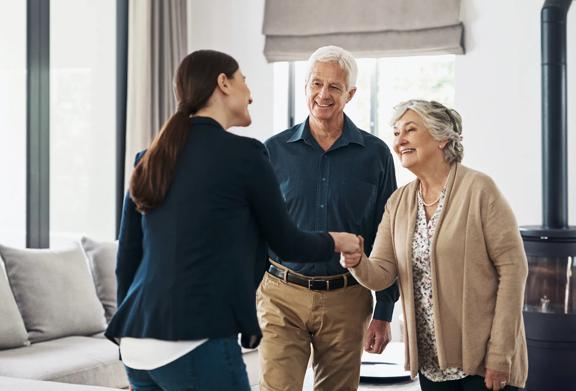Smiling senior couple greeting a professional woman with a handshake inside a modern living room.