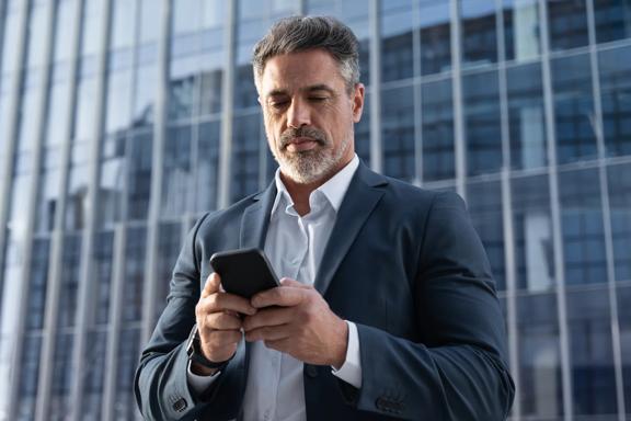 Professional man looking at smartphone outside modern office building