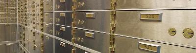 Rows of metallic safe-deposit boxes with numbered brass plates and keyholes inside a secure vault.