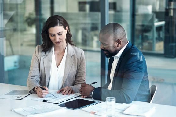 Collaborative business discussion with two people reviewing paperwork at an office table.