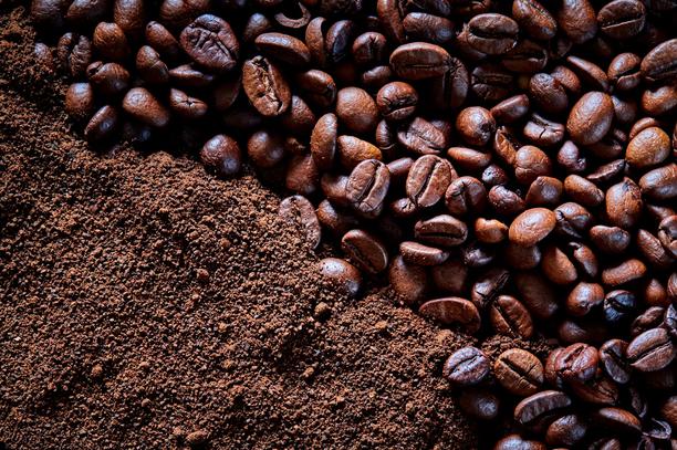 Close-up of roasted coffee beans scattered across a layer of finely ground coffee, showing rich brown textures and varying bean sizes.