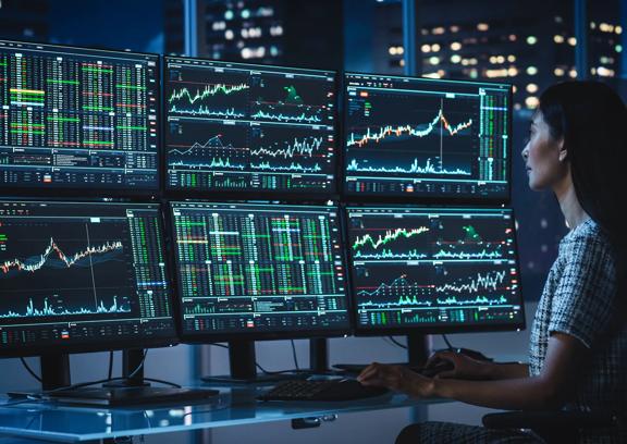 Woman looking at 6 screens of financial data