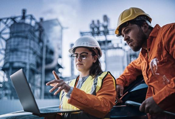 Business professionals reviewing risk data on laptop in industrial setting