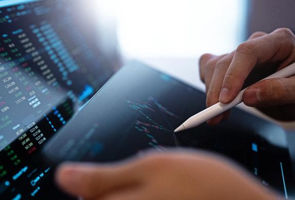 Close-up de mãos usando uma caneta stylus para analisar gráficos do mercado de ações em um tablet digital