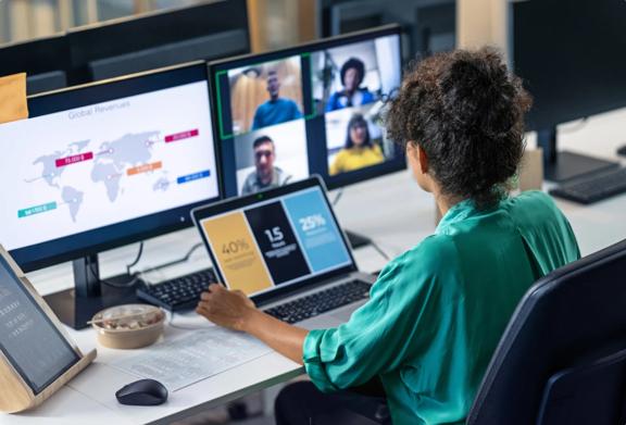Business professional attending a virtual team meeting while analyzing data on multiple screens