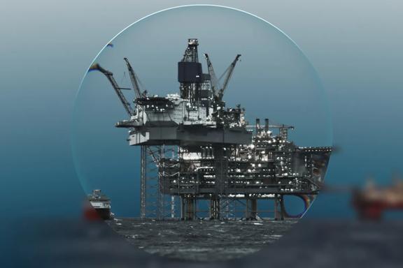 Magnifying lens on offshore oil platform on a teal background