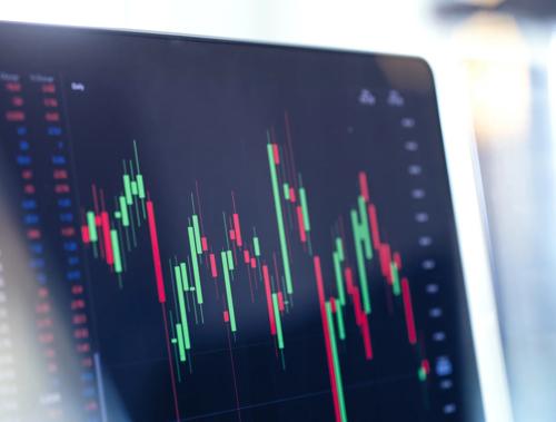 Laptop screen displaying a candlestick chart with red and green bars indicating stock market activity