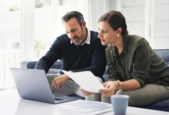 Middle-aged couple reviewing financial documents together at home using a laptop