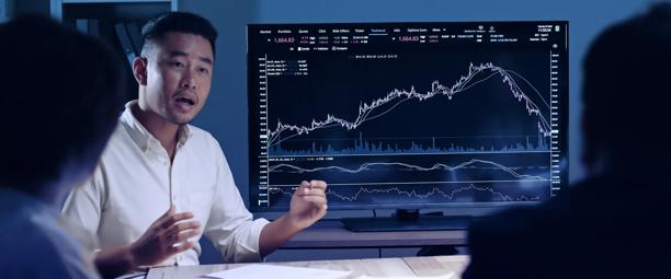 Men talking in front of a screen showing a financial chart
