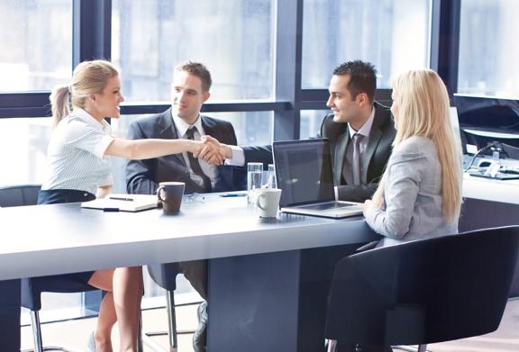 Business professionals in formal attire shaking hands across a conference table during a successful meeting