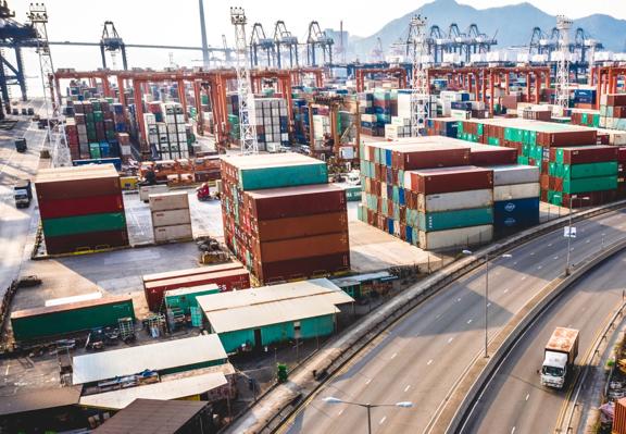 Shipping containers stacked at a busy port with cranes and transport infrastructure