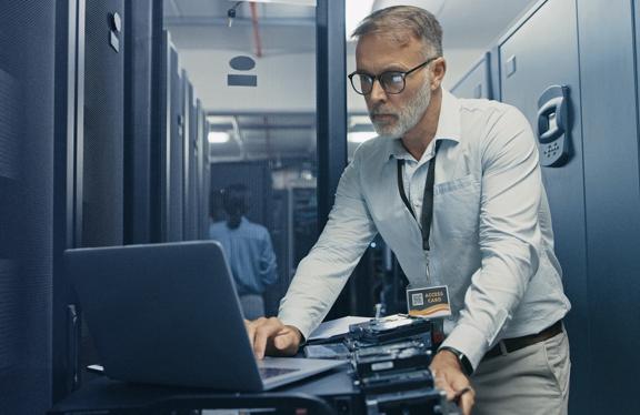 Especialista em TI trabalhando em um laptop dentro de um data center com racks de servidores ao redor