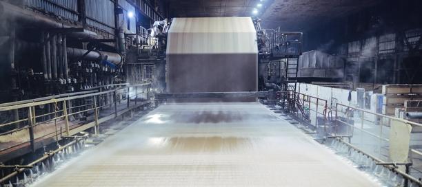 Industrial paper mill with large machinery processing sheets of paper.