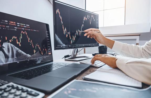 Trader analisando tendências do mercado de ações em telas duplas em um ambiente de escritório moderno.