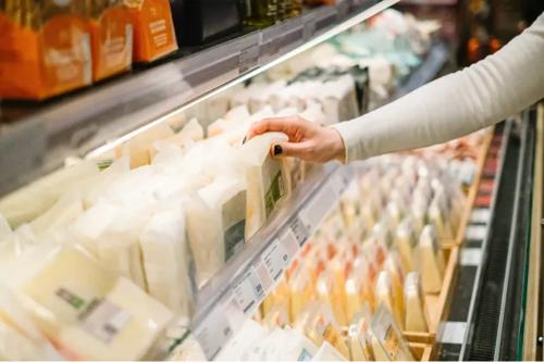 Seleção manual de produtos lácteos embalados em uma prateleira refrigerada de supermercado.