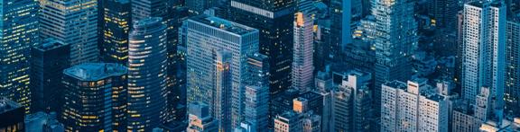 Aerial view of the New York City skyline at dusk featuring modern skyscrapers with glowing office lights.