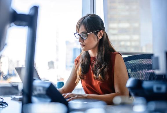 Focused businesswoman working on a laptop at her desk in a modern office with city views
