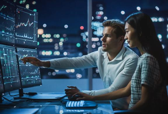 Man and woman looking at multiple screens of financial data