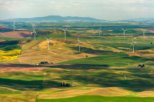 Aerial view of wind turbines spread across rolling green and golden farmland in a rural landscape.