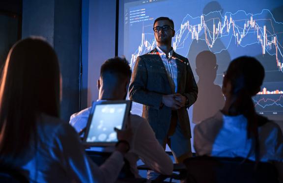 Professional man standing in front of projection of financial chart with an audience