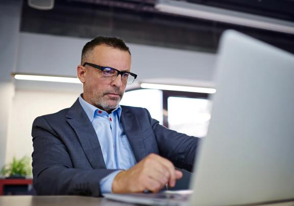 Focused businessman in formal attire working on a laptop in a modern office setting