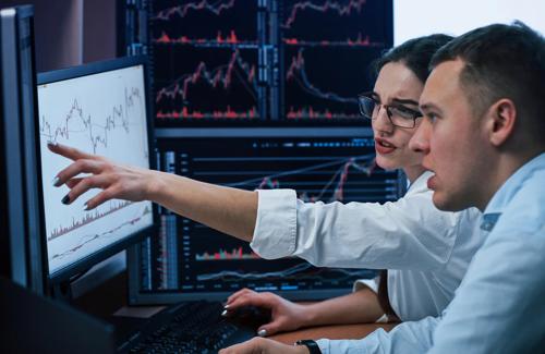 Financial analysts examining stock market data and trends on multiple computer monitors