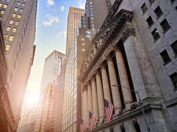 Facade of the New York Stock Exchange building on Wall Street with American flags


