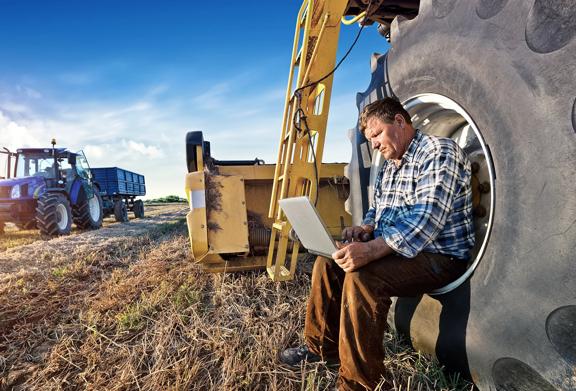 Farmer sitting in a tractor wheel looking at Fertilizers Market Intelligence on his laptop