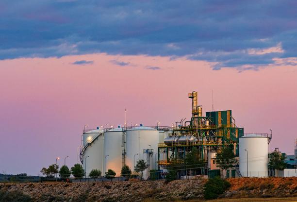 Industrial oil or chemical storage facility with large white tanks and processing infrastructure at sunset.