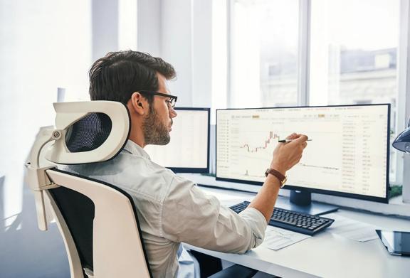 Profissional analisando dados financeiros em vários monitores de computador em um escritório moderno.