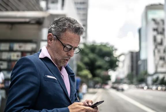 Homem de negócios usando smartphone em uma avenida movimentada da cidade.