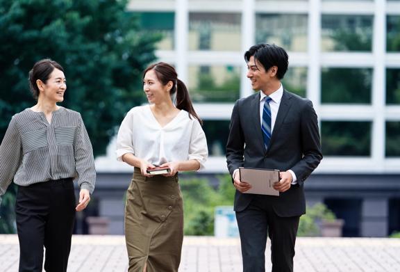 Three professionals walking outdoors near an office building, one holding a tablet.