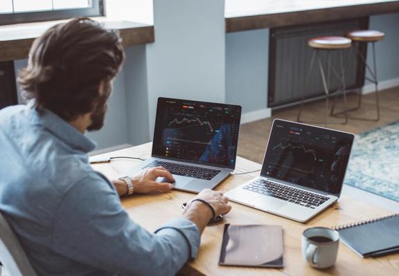 Trader analysing financial charts on dual laptops at a modern workspace desk