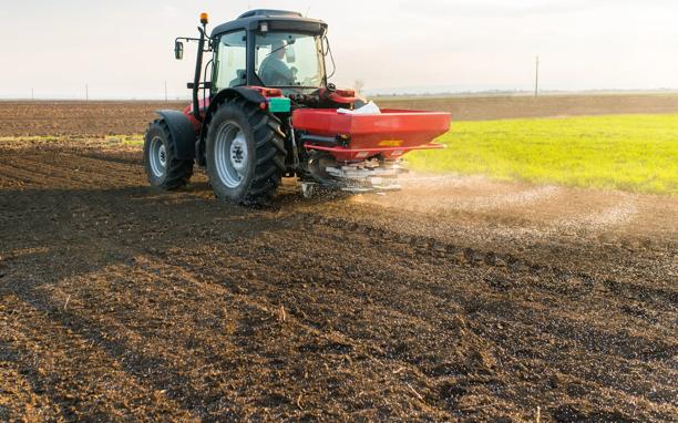 Red tractor spreading fertilizer across a plowed agricultural field to prepare soil for planting