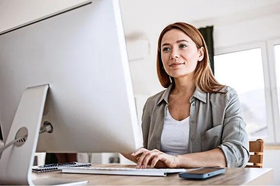 Pessoa trabalhando em computador desktop sobre mesa, com smartphone ao lado.