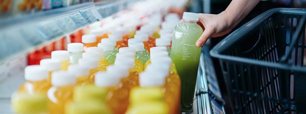 Person picking a green juice bottle from a refrigerated shelf filled with colorful beverages in a grocery store