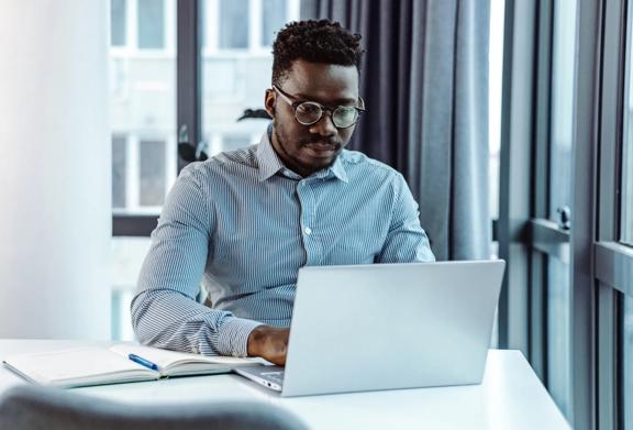 Man wearing glasses working on laptop by window