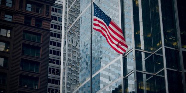 United States flag displayed outside modern office buildings in a financial district. Economic and financial market concept representing the US economy, global business, investment markets, and corporate finance.
