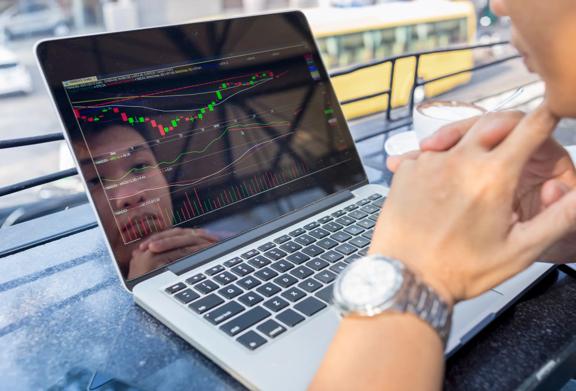Person analyzing stock market charts on a laptop screen in an outdoor setting