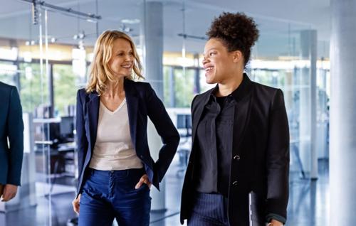 Two smiling businesswomen walking and talking in a modern office environment