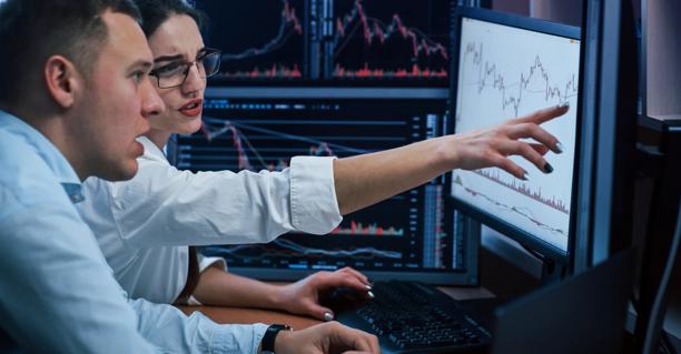 Two financial analysts reviewing charts and market data on multiple computer monitors