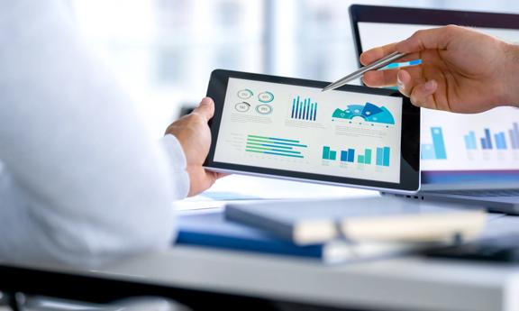 Dois homens de negócios se reúnem e analisam dados financeiros, tabelas e gráficos em um tablet digital e um laptop.