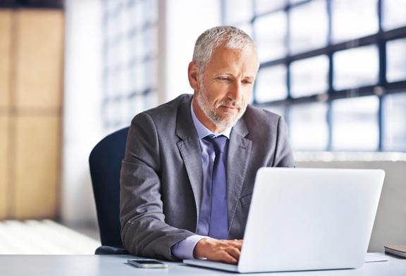 Senior businessman in a suit working on a laptop in a modern office setting