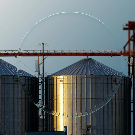 Agricultural grain storage silos and industrial grain handling equipment shown through a reflective glass sphere against a blue gradient background.