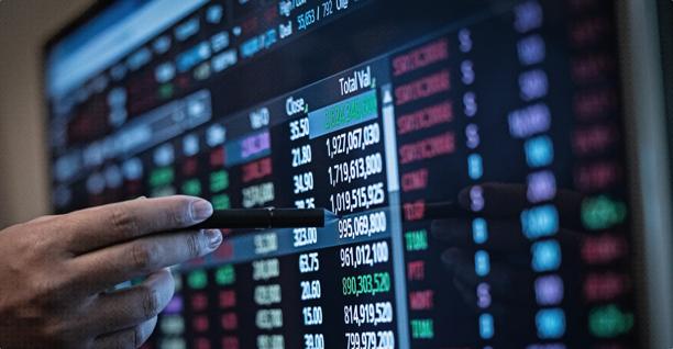 Close-up of a hand pointing at financial data on a digital stock market display